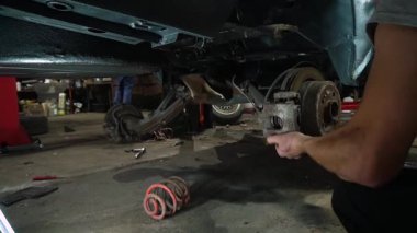 Özel egzoz sistemi ve egzoz manifoldu araba genç tamirci tamir ve eski gri bir araba monte bir trafik kazası sonra arka süspansiyon yeni sessiz bloklar baskı arka süspansiyon onarım ve yeni fren diskleri yükleme