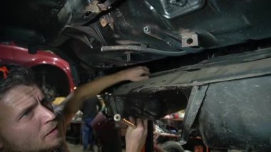 Özel egzoz sistemi ve egzoz manifoldu araba genç tamirci tamir ve eski gri bir araba monte bir trafik kazası sonra arka süspansiyon yeni sessiz bloklar baskı arka süspansiyon onarım ve yeni fren diskleri yükleme