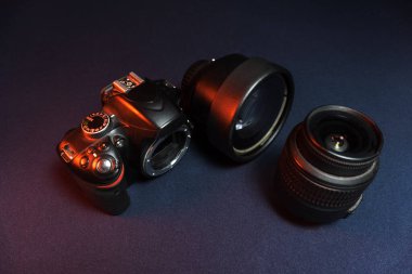 Kullanılmış, yeni değil, siyah SLR kamera. Stüdyoda kırmızı ışıkta iki lensli bir tripodun üzerinde.