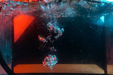 Su dokusu gürleyen kaos içinde hava kabarcıkları yaratıyor mavi ve kırmızı ışıkta dışarı kaçıyorlar.