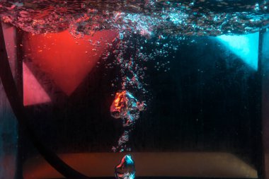 Su dokusu gürleyen kaos içinde hava kabarcıkları yaratıyor mavi ve kırmızı ışıkta dışarı kaçıyorlar.