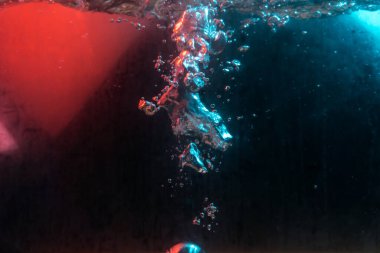 Su dokusu gürleyen kaos içinde hava kabarcıkları yaratıyor mavi ve kırmızı ışıkta dışarı kaçıyorlar.