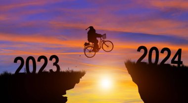 Mutlu Noeller ve 2024 yılına hoş geldiniz. Siluet Noel Baba 2023 'ten 2024' e kadar Sunset ve Twilight Sky arka planında bir bisikletle boşluktan atlıyor..