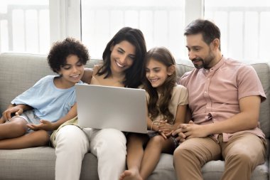Neşeli Latin ebeveynler ve iki tatlı çocuk dizüstü bilgisayarlarında sohbet ediyorlar, birlikte kanepede dinleniyorlar, bilgisayar tutuyorlar, internet iletişiminin keyfini çıkarıyorlar, online eğlence.