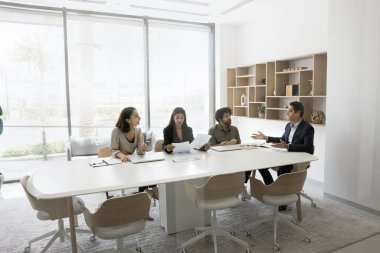 Toplantı odasında beyin fırtınası yapan, modern ofisteki büyük müzakere masasında konuşan dört kişilik çok ırklı bir iş ekibi. Ortaklar işbirliği, ortaklık, yatırım konularını tartışıyor. Cam manzaralı.