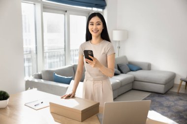 Akıllı telefondan lojistik uygulama kullanan, ulaşım hizmeti veren, paketi aldıktan sonra web mağazasına geri bildirim yapan, kameraya bakan, gülümseyen mutlu güzel Çinli kız.