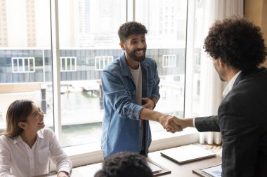 Neşeli proje lideri başlangıç satışı yapıyor, iş toplantısında yatırımcılara el sıkışma yapıyor. Başarılı genç Arap girişimci eşiyle tokalaşıyor, gülümsüyor, gülüyor.