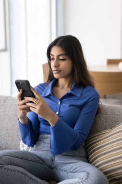 Akıllı telefon tutan, evdeki koltukta dinlenen, sosyal medyayı karıştıran modern kablosuz teknoloji kullanan, online uygulama, daktilo kullanan güzel, genç Hintli bir kadın. Dikey çekim