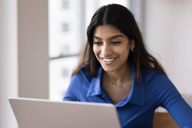Mutlu genç Hintli serbest çalışan ev işyerindeki dizüstü bilgisayarda çalışıyor, dişlek gülümsemeyle ekrana bakıyor, video konuşmalarıyla konuşuyor, profesyonel internet iş iletişiminin keyfini çıkarıyor.