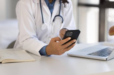 İş yerinde akıllı telefon kullanan, dizüstü bilgisayarda oturan, tıbbi profesyonel uygulamalarla çalışan, hastalarla sohbet eden, internette danışmanlık yapan genç kadın doktorların elleri.