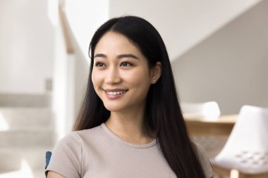 Neşeli, güzel, genç, Asyalı, siyah düz saçlı, uzun saçlı, dişlek gülümsemesi ve düşünceli yüzüyle pencereye bakan bir kadın. Mutlu yirmili yaşlarda kadın güzellik mankeni portresi