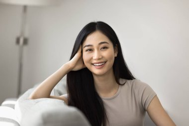 Mutlu 20 'li yaşlardaki Asyalı kız evde portre için poz veriyor, rahat bir koltukta oturuyor, dişlek gülümsemesiyle kameraya bakıyor, gülüyor, el ele tutuşuyor. Güzel genç bir kadınla görüntülü konuşma ekranı