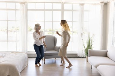 Modaya uygun, ferah oturma odasında aktif aile dansı, anne ve genç kız müziğe taşınıyor, eğleniyor, kaygısız hissediyor ve birlikte favori şarkı ve zamanın tadını çıkarıyor. Evde aile eğlencesi.