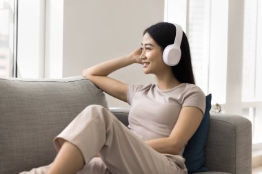 Kablosuz kulaklık takan, pencereden bakan, çevrimiçi müzik listesinden şarkılar dinleyen, internet hizmeti, medya uygulaması, evde dinlenen,