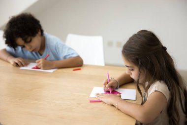 Odaklanmış erkek kardeş ve kız kardeş el yapımı tebrik kartına kırmızı kalpler çiziyor, anneler günü, doğum günü için hediyeler hazırlıyor, masada oturuyor, yaratıcılık eğitimi alıyor, ilham veriyor, sanatsal beceriler kazanıyor.