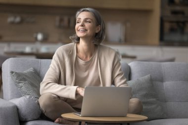 Mutlu olgun bir kadın evde vakit geçirir, kanepeye oturur, kafasını çevirir, elektronik hizmetlerden zevk alır e-alışveriş siteleri kullanır, internetten alışveriş yapar, mesaj bekler, iletişim için modern teknoloji ve internet kullanır.