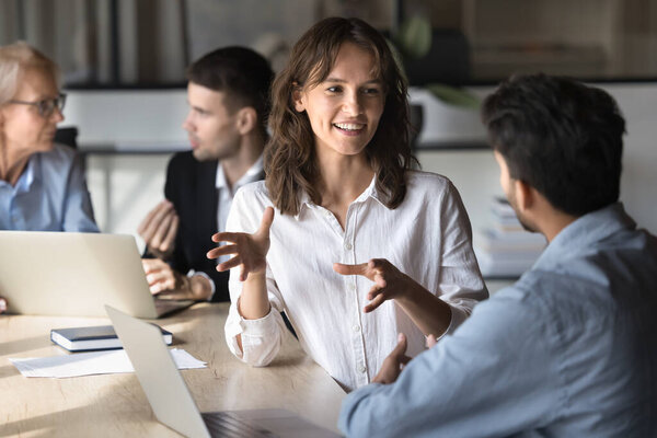 Positive Caucasian project manager woman talking to Indian coworker, business partner at office meeting, discussing collaboration, moving hands, smiling, explaining ideas, planning work process