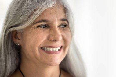 Uzun gri saçlı, doğal makyajlı, dişlek gülümsemesiyle yüzünü çeviren mutlu yaşlı Latin kadın. Yaşlı kadın modelin yüzü yaşlı güzelliği, diş bakımını teşvik ediyor. Portreyi kapat