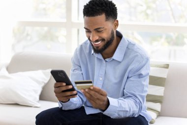 Neşeli genç Afrikalı müşteri online alışveriş yapıyor, kredi kartıyla ödeme yapıyor, web mağazası ekommerce hizmeti kullanıyor, banka hesabı bakiyesini kontrol ediyor.