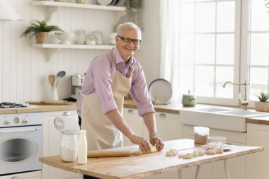 Yaşlı adam hamur yoğuruyor tatilde ev yapımı hamur işleri hazırlıyor, sabahları mutfakta aileye sürpriz yapıyor. Emeklilik hobisi, yemek pişirme süreci, doğal ekolojik ürünler, aşçılık