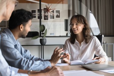 İş görüşmelerine katılan farklı iş arkadaşları iş projelerini tartışıyor. Erkek Hintli işçi ve genç bayan patron toplantı masasında konuşuyor, gülümsüyor, beyin fırtınası yapıyor.