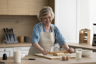Çekici, yaşlı kadın ev hanımı önlük giyer. Mutfakta elinde oklavayla durur, hamur işlerini düzleştirir. Aile turtası ya da pastaya hazırlanır, gülümseyerek evde yemek pişirir.