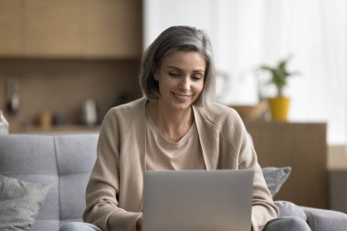 Kaygısız, orta yaşlı bir kadın evde rahatlar, hafta sonunu evde dizüstü bilgisayarla geçirir, ekrana bakar, sohbet eder, çevrimiçi iletişimden zevk alır, internete göz atar, modern uygulama kullanır, alışveriş yapar.