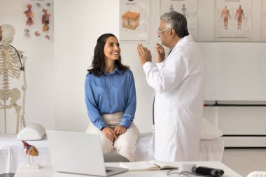 Hintli kıdemli doktor, pozitif genç hasta kadını muayene ediyor klinikteki tıbbi kanepede oturuyor, sağlık şikayetlerini tartışıyor, tedavi hakkında danışmanlık yapıyor.