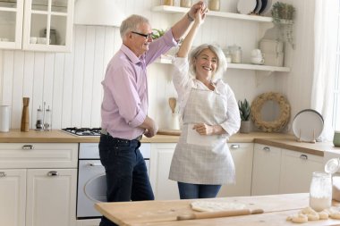 Olgun bir çift, kıdemli bir baba ve olgun bir kız el ele tutuşuyor, dönüyor, birlikte eğleniyorlar hafif modern ev mutfağında birlikte vakit geçiriyorlar ve evde aile tatili üzerine ev yapımı hamur işleri hazırlıyorlar.