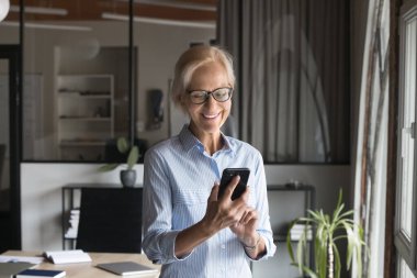 Başarılı, olgun bir iş kadını akıllı telefonuyla internet üzerinden iş görüşmesi yapıyor, cep telefonuyla sohbet ediyor, mesaj yazıyor, gülümsüyor, gülüyor.