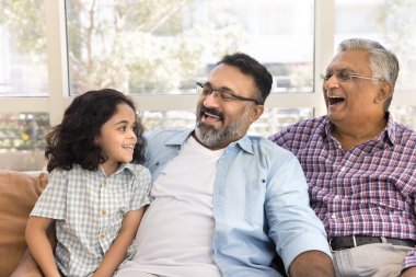 Neşeli Hintli büyükbaba, büyük dede küçük tatlı torunu izliyor, aile eğlencesinin tadını çıkarıyor, birlikte çocuk bakıcılığı yapıyor, kanepede oturuyor, sarılıyor, konuşuyor, gülüyor, eğleniyor.