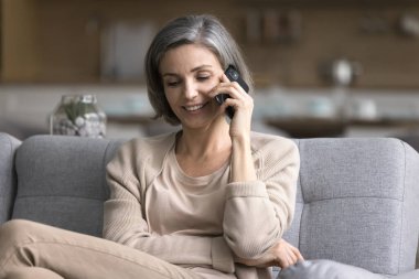 Kaygısız, çekici, orta yaşlı bir kadın oturma odasında kanepede vakit geçirir, akıllı bir telefon tutar, telefon eder, arkadaş ya da aileyle hoş sohbetler yapar, uzaktan iletişimin tadını çıkartır.