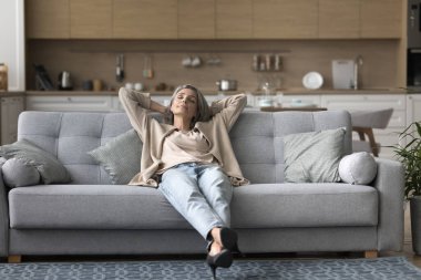 Huzurlu orta yaşlı bir kadın oturma odasında rahat bir koltukta oturur, elleri başının arkasına yaslanır, tembelce hafta sonunun tadını çıkarır, modern evde gündüz uykusunun tadını çıkarır. Yorgunluk nöbeti, mola, rahatlama