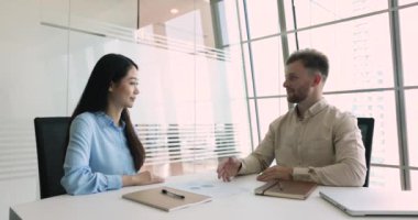 Muhtelif meslekdaşlar toplantı masasında oturup anlaşma, takım çalışması, tokalaşma, gülümseme hakkında konuşuyorlar. Mutlu Asyalı şirket lideri kadın iş ortağına el sıkışıyor.