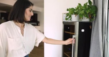 Genç ve çekici Meksikalı kadın içecek dolabını açar ve sıcak yaz gününde bir şişe bira içer, hafta sonları evde güzel vakit geçirir. İçecekleri soğutmak, depolamak ve soğutmak için modern aygıt