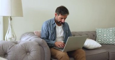 Ciddi, olgun Portekizli adam oturma odasındaki kanepede dizüstü bilgisayarda çalışıyor, tele-posta yazma, e-posta yazma, uzaktan iş çözme, mesajlaşma yoluyla kurşun yazışmaları modern aygıtları kullanarak