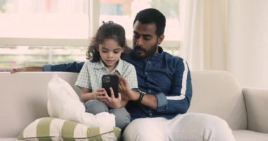 Sevgi dolu Hintli baba küçük sevimli oğluna modern akıllı telefon kullanmayı, yeni mobil uygulama öğrenmeyi evdeki kanepede dinlenerek online oyunlar oynamayı öğretiyor. Genç nesil ve kablosuz teknoloji, aşırı internet kullanımı