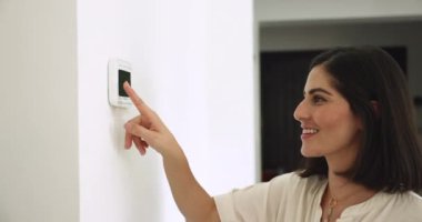 Genç, güzel Latin bir kadın düğmeye basıyor, akıllı ev sistemi kuruyor, modern güvenlik ekipmanları ya da alarm kontrol panelini kullanarak ısıyı düzenliyor. Teknoloji, güvenlik, konfor hayatı