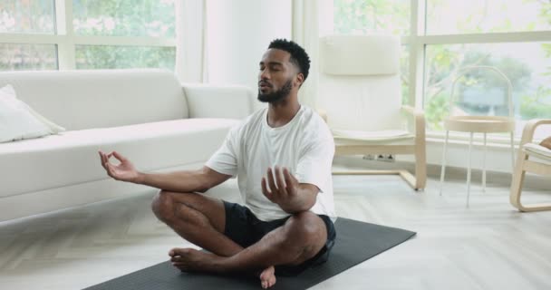 在练习冥想时 身穿运动服的非洲年轻人在回家时盘腿坐在垫子上做瑜伽练习 然后用放松练习来完成训练 在冥想练习过程中 他们深深地吸气和呼气 — 图库视频影像