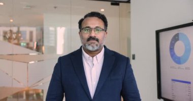 Resmi takım elbiseli yetişkin Hintli işadamı, kollarını kavuşturmuş, kameraya bakıp gülümsüyor, güven ve liderlik yayıyor, mali ve muhasebe alanında güvenilirlik ve uzmanlık tasvir ediyor.