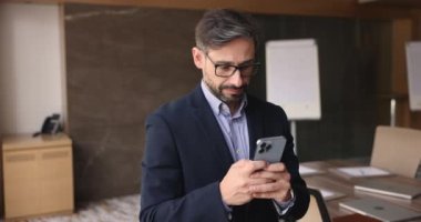 Olgun Portekizli işadamı iş yerinde modern cep telefonu kullanıyor, akıllı telefon tutuyor, e-postaları kontrol ediyor, internette geziniyor, mesajları kontrol ediyor, sorunları uzaktan çözüyor, yeni cep telefonu uygulamaları öğreniyor.