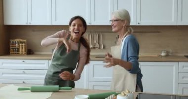 İki yaşlı ve genç kadın, yaşlı anne genç yetişkin kızı favori müzikle dans ediyor, popüler şarkı söylüyor aile hafta sonundan zevk alıyor, iyi ilişkiler kuruyor.