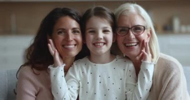 Sevgi dolu anne ve büyük anneyle kameraya poz veren küçük sevimli kız gülüşü. Evdeki kanepede oturmuş kameraya bakarak gülen çok nesilli aile fotoğrafının yakın çekimi. Aşk, bağ