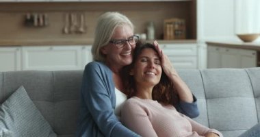 Yaşlı kadın, yetişkin kızına sarılıyor ve sıcak oturma odasında, iyon rahat kanepesinde oturarak şefkatin ve şefkatin tadını çıkarıyor. Çok nesilli aile bağları ve bağları, annelik, anlayış