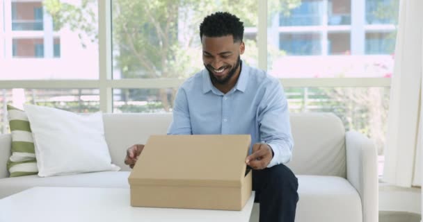 Задоволений Африканський Чоловік Електронний Клієнт Відкриває Посилку Товарами Доставленими Вдома — стокове відео