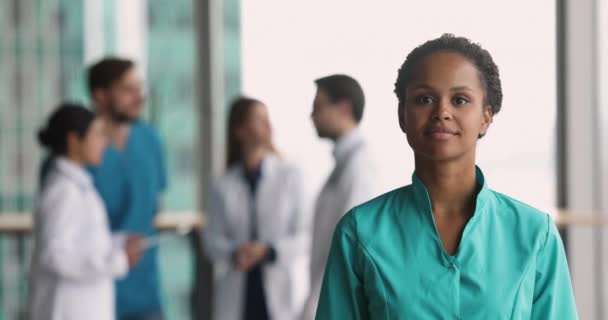 グリーンユニフォームで笑顔のアフリカの看護師を介して 心臓のシンボルを臨床オフィスのカメラポーズを見て 保険に専門的な医療サービスを提供します — ストック動画