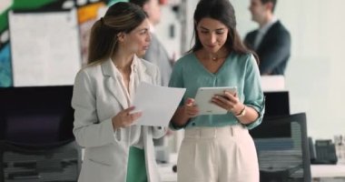 İki çekici iş kadını iş arkadaşı sözleşme detaylarını tartışıyor, gülümsüyor, sohbet ediyor modern ofiste koridorda yürüyor, fikirleri, fikirleri, çözümleri paylaşıyor, takım çalışması ve iş akışına karışıyor.