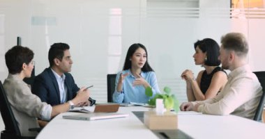 Olumlu, güzel, genç Asyalı takım lideri kadın çok ırklı iş arkadaşlarıyla konuşuyor, çeşitli takımlara yaratıcı fikirleri anlatıyor, büyük toplantı masasında konuşuyor, takım çalışmasının keyfini çıkarıyor.