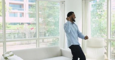 Komik genç Afrikalı adam oturma odasında tek başına dans ediyor, en sevdiği parçayı söylüyor, havalı popüler şarkı söylüyor hafta sonları yalnız başına modern oturma odasında eğleniyor. Hobi, hayatın tadını çıkar.