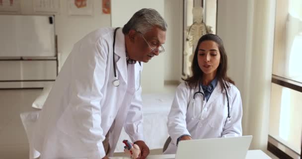 Két Többnemzetiségű Orvos Beszél Laptopon Online Tartalmakat Néznek Orvosi Teszteredményekről — Stock videók
